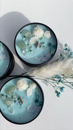 three blue bowls with white flowers in them on a table next to feathers and plants