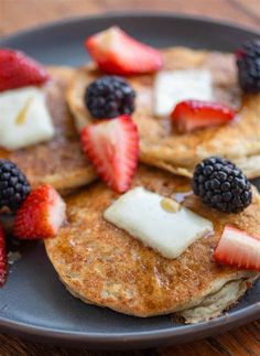 pancakes topped with fruit and butter on a black plate, sitting on a wooden table