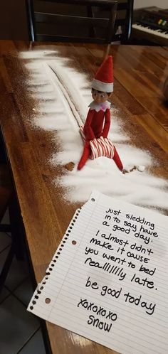 an elf is sitting in the snow next to a note