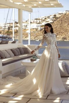 a woman in a wedding dress standing on a patio near a couch and table with pillows