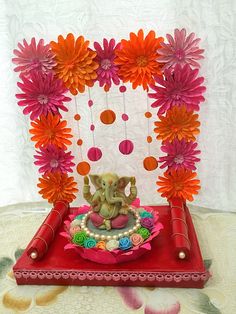 an elephant statue sitting on top of a red tray surrounded by flowers and paper decorations