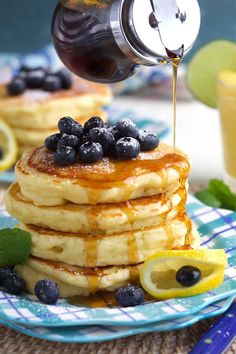 a stack of pancakes with syrup being drizzled over them and topped with blueberries