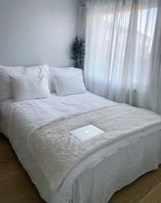 a bed with white sheets and pillows in front of a window, next to a laptop computer