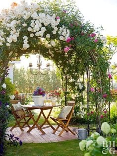 a table and chairs under an arch covered in flowers