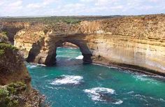 the ocean is blue and green with waves coming in from it, near an arch shaped rock formation