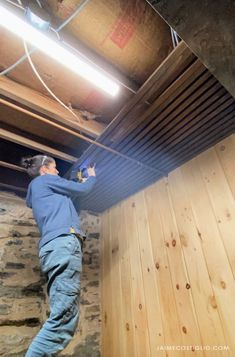 a man is working on the ceiling in his basement with wood planks and exposed pipes