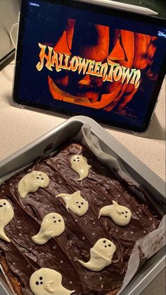 a cake in a pan with chocolate frosting and ghost decorations on it, sitting on a table