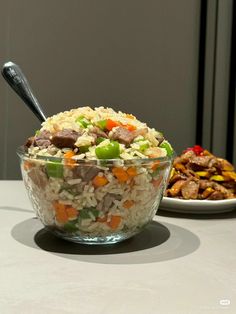 a bowl filled with rice and vegetables next to a plate full of food on a table