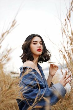 a woman standing in tall grass with her hands on her hips and looking off to the side