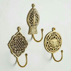 three gold colored metal hooks with intricate designs on each hook and an ornate design on the back