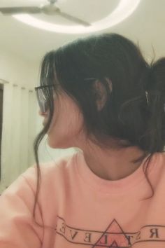 a girl with glasses and a pink shirt is looking at her cell phone in the mirror