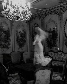 a black and white photo of a woman standing in front of a chandelier