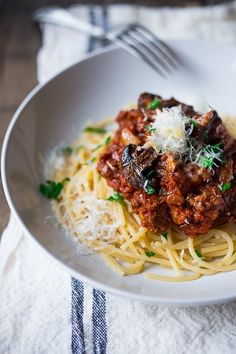 a white bowl filled with pasta and meat sauce on top of a table next to a fork