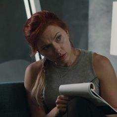 a woman with red hair sitting on a couch looking at a piece of paper in her hand