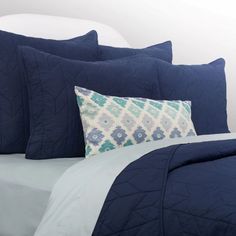 a bed with blue comforters and pillows on top of it, in front of a white headboard