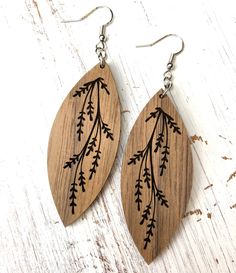 wooden earrings with black leaves on them sitting on top of a white wood table next to a pair of silver ear wires