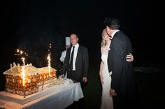 two men and a woman standing in front of a cake with lit candles on it