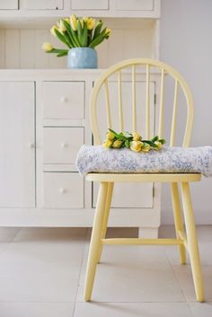 a yellow chair sitting in front of a white cabinet and vase with tulips on it