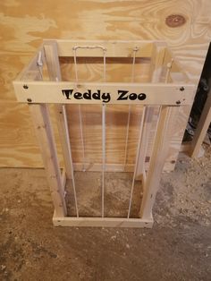 a wooden cage with the words teddy zoo written on it in black lettering, sitting next to some wood planks