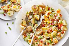 two plates filled with potato salad on top of a white table next to silverware