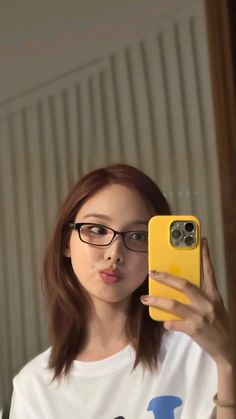 a woman wearing glasses taking a selfie with her cell phone in front of her