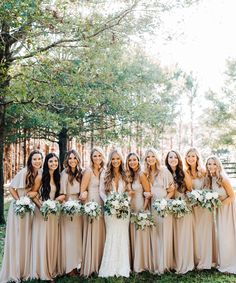 a group of women standing next to each other in front of trees and grass with bouquets