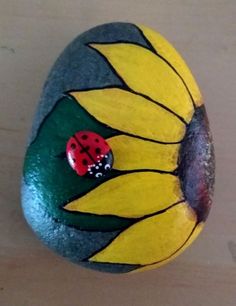 a painted rock with a ladybug sitting on it's back and yellow petals