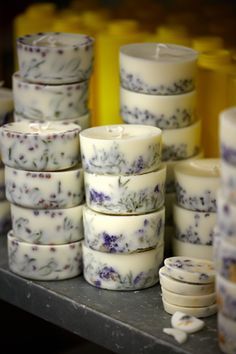 many white candles with purple flowers on them are stacked up in front of each other