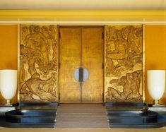 an elaborately carved wooden door with two lamps in the foreground and on the far side