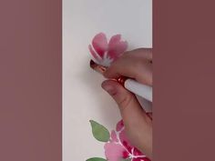 someone is painting flowers on the wall with pink and green leaves in front of them