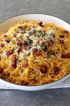 a white bowl filled with spaghetti and sausages on top of a table next to a napkin