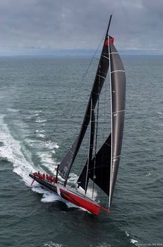 a red and black sailboat in the ocean with people on it's side