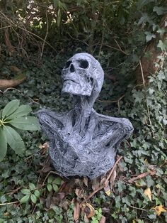 a statue of a skeleton sitting in the middle of some leaves and bushes with trees behind it