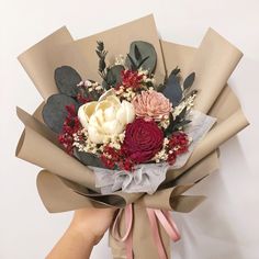 a bouquet of flowers is wrapped in brown paper and being held by someone's hand