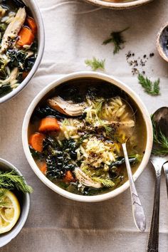 two bowls filled with soup next to silver spoons and lemon slices on a table