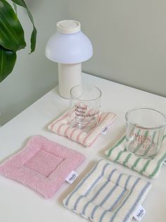 towels and glasses on a table next to a lamp, vase with green plant in it