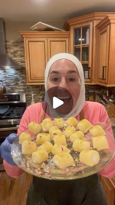 a woman in a kitchen holding a platter full of food and making a funny face