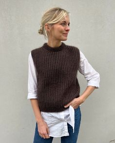 a woman standing in front of a white wall wearing a brown knitted sweater vest