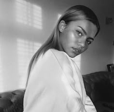 a black and white photo of a woman sitting on a couch looking at the camera