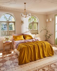 a bed with yellow sheets and pillows in front of two arched windows on the wall