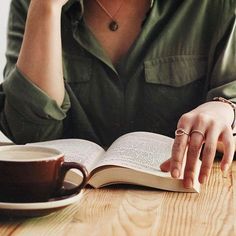 a woman sitting at a table with an open book and coffee cup in front of her