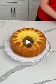 a bundt cake sitting on top of a white plate next to a woman in a red shirt