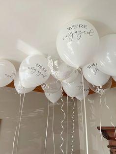 white balloons with we're engaged written on them hanging from a ceiling in a room