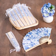 a blue and white fan next to a vase with flowers in it on a wooden table