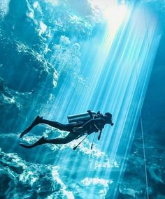 a person is diving in the water with their scuba gear on and there is light coming from behind them