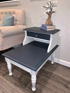 a white and black end table with a book on it next to a beige chair