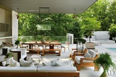 an outdoor living area with couches and tables next to a pool surrounded by trees