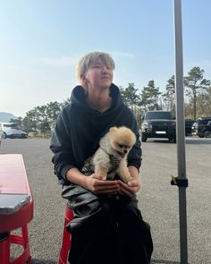 a woman is holding a small dog in her lap while sitting on a red bench