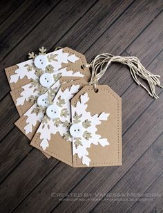 four tags with white snowflakes on them sitting on a wooden table next to string and twine