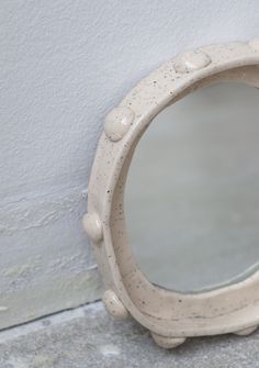 a white round mirror sitting on the side of a wall next to a cement floor